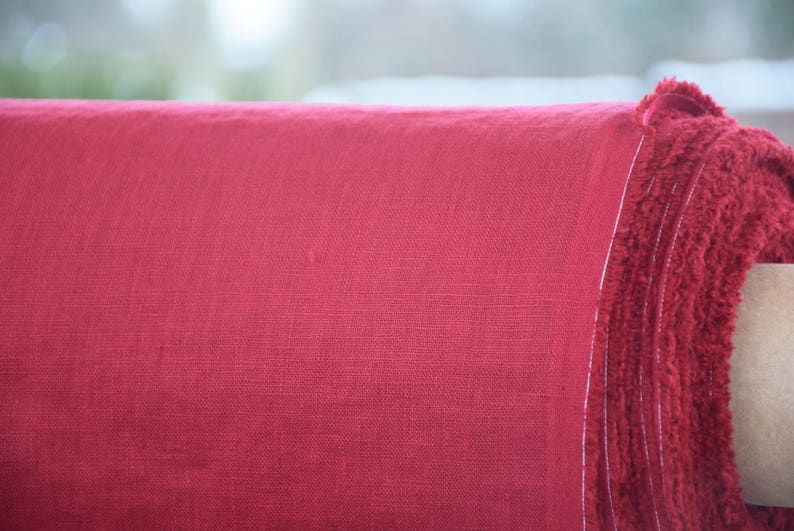 May include: Close-up of a roll of red linen fabric. The fabric has a textured, woven appearance.