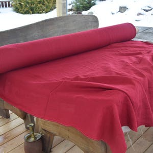 May include: A roll of red linen fabric is unfurled on a wooden table. The fabric is smooth and has a subtle texture.