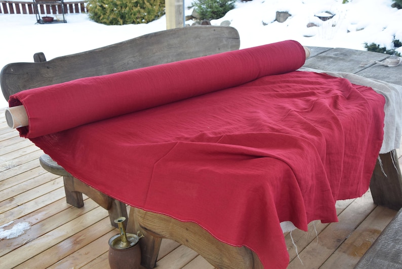 May include: A roll of red linen fabric is unfurled on a wooden table. The fabric is smooth and has a subtle texture.