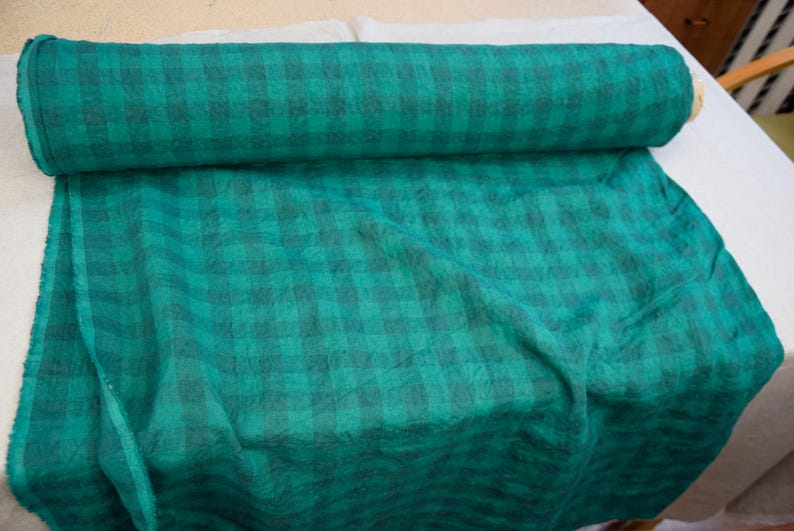 May include: A roll of teal fabric with a dark teal plaid pattern. The fabric is partially unrolled, revealing the plaid design. The fabric is likely used for sewing, crafting, or home decor projects.