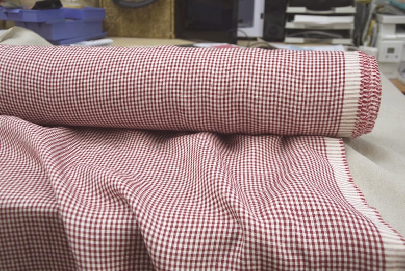 May include: A roll of red and white checkered fabric, partially unrolled to reveal more of the pattern. The fabric has a classic gingham design, suitable for various sewing and crafting projects. The fabric is likely cotton or a similar material.