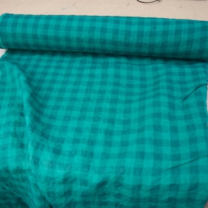May include: A roll of teal fabric with a checkered pattern. The fabric is unrolled on a white surface, revealing the same teal and checkered design. The fabric appears to be a medium weight material.