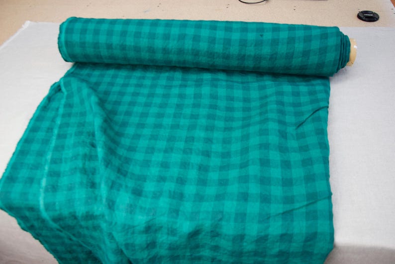 May include: A roll of teal fabric with a checkered pattern. The fabric is unrolled on a white surface, revealing the same teal and checkered design. The fabric appears to be a medium weight material.
