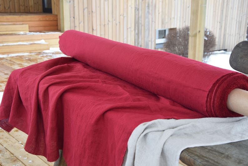 May include: A roll of red linen fabric on a table. The fabric is folded and has a natural texture.