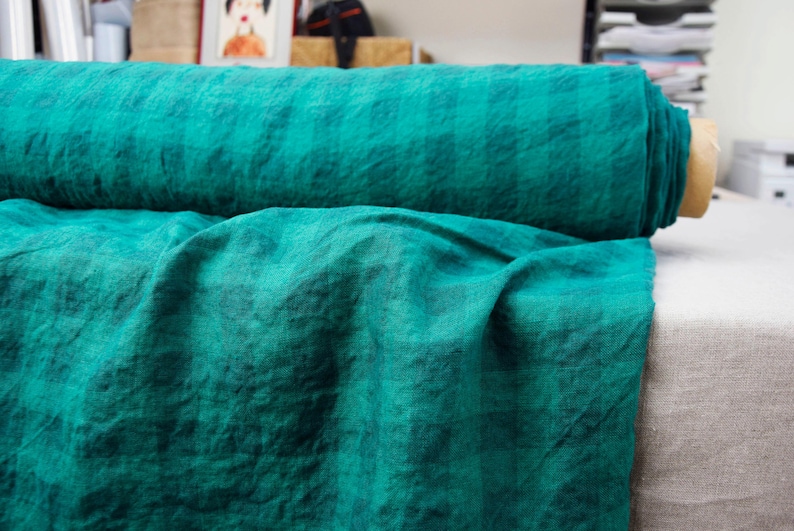 May include: A roll of teal-colored fabric, partially unrolled to reveal the texture. The fabric is a solid teal color with a slightly wrinkled appearance. The roll is resting on a neutral-colored surface.