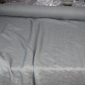 May include: A roll of light blue fabric with a linen texture. The fabric is laid out flat and is folded in half.
