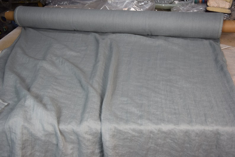 May include: A roll of light blue fabric with a linen texture. The fabric is laid out flat and is folded in half.