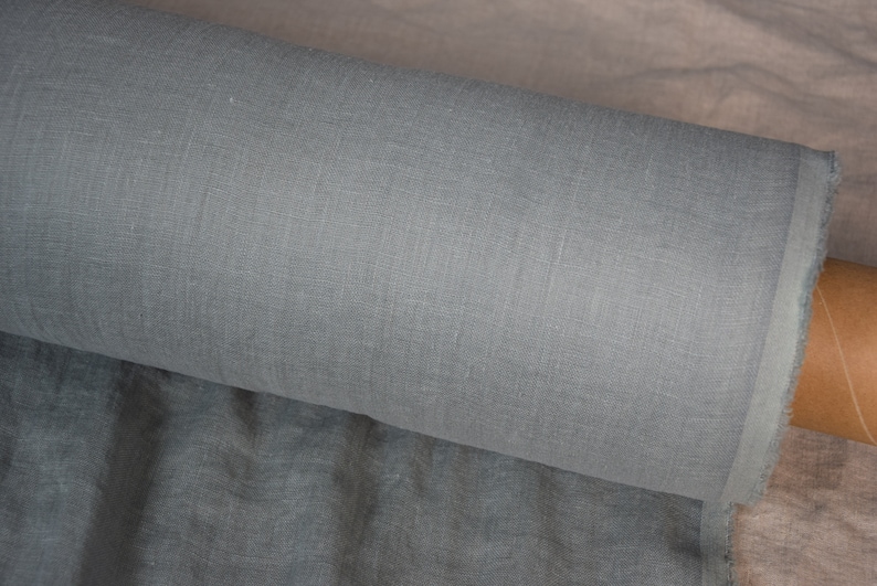 May include: A roll of light gray linen fabric. The fabric has a subtle texture and is perfect for sewing projects.