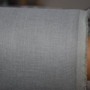 May include: Close-up of a light gray linen fabric with a slightly textured surface. The fabric is rolled up and the edge is visible.