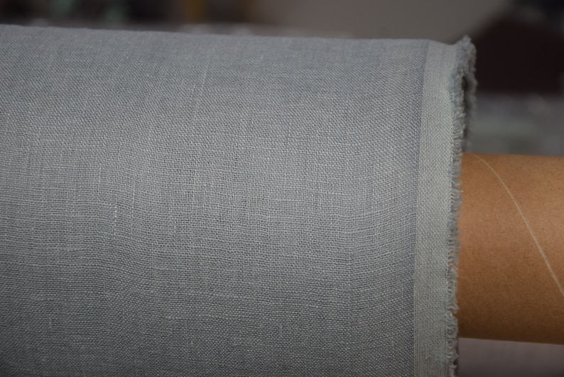 May include: Close-up of a light gray linen fabric with a slightly textured surface. The fabric is rolled up and the edge is visible.