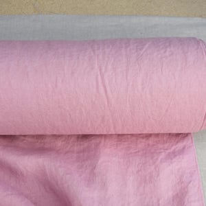Puede incluir: Se muestra un rollo de tela rosa claro, probablemente de algod&oacute;n o lino. La tela est&aacute; enrollada firmemente, revelando su textura y color. El rollo se coloca sobre un fondo neutro, resaltando el color y la textura de la tela.