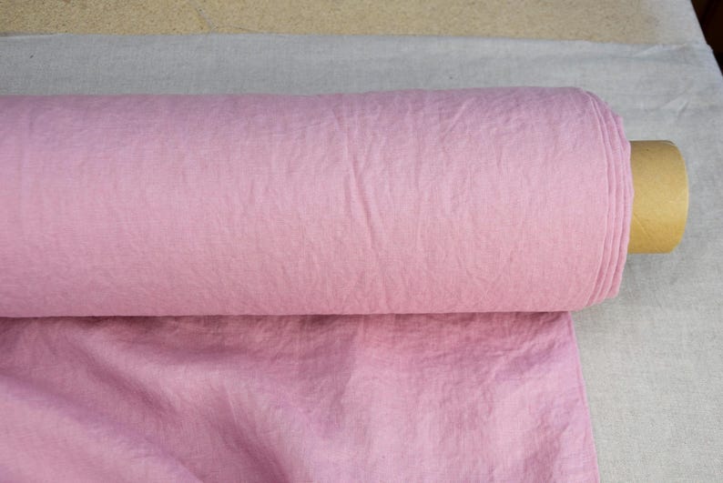 Puede incluir: Se muestra un rollo de tela rosa claro, probablemente de algod&oacute;n o lino. La tela est&aacute; enrollada firmemente, revelando su textura y color. El rollo se coloca sobre un fondo neutro, resaltando el color y la textura de la tela.
