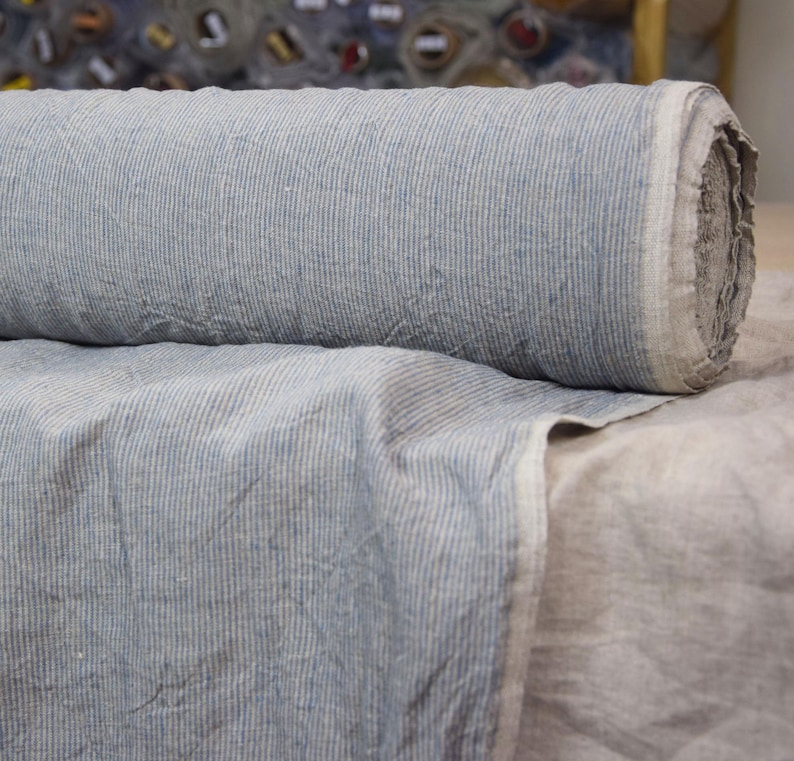 Puede incluir: Un rollo de tela de lino a rayas azules y blancas. La tela tiene un aspecto texturizado y ligeramente arrugado.