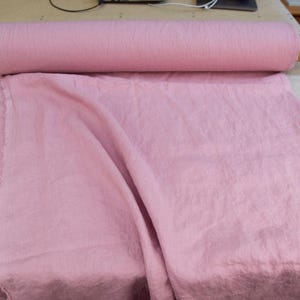 Puede incluir: Un rollo de tela rosa claro est&aacute; sobre una mesa, con una parte de la tela desenrollada. La tela tiene un aspecto suave y texturizado. El rollo mide aproximadamente 76 cm de largo.