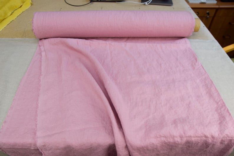 Puede incluir: Un rollo de tela rosa claro est&aacute; sobre una mesa, con una parte de la tela desenrollada. La tela tiene un aspecto suave y texturizado. El rollo mide aproximadamente 76 cm de largo.
