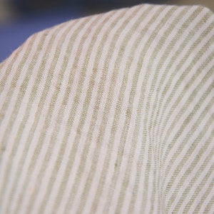 May include: Close-up of a white and beige striped fabric with a subtle texture. The fabric has a woven appearance and a soft, natural feel.