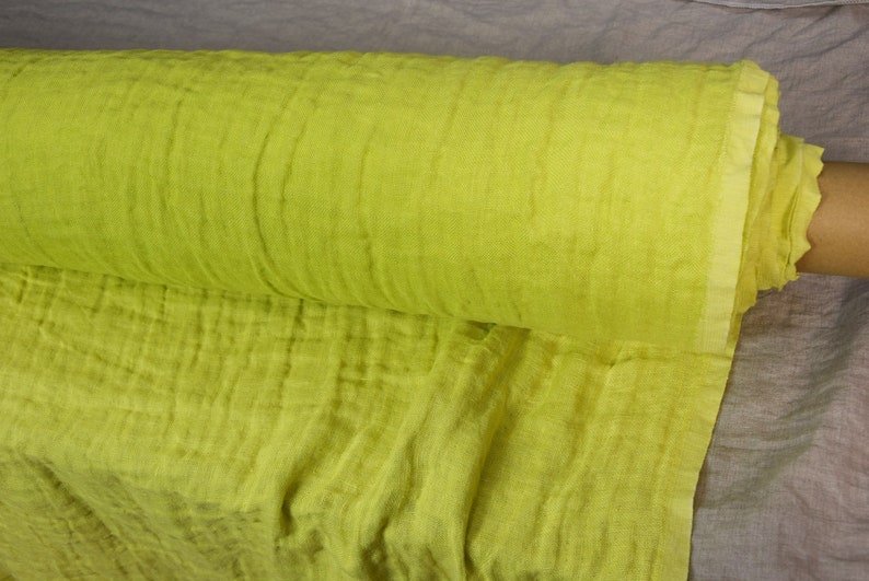 May include: A roll of bright yellow fabric with a crinkled texture. The fabric is folded and rolled up, and the end of the roll is visible.