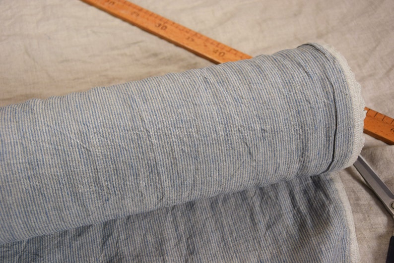 Puede incluir: Un rollo de tela rayada azul y blanca. La tela tiene una textura de lino y est&aacute; doblada por la mitad.