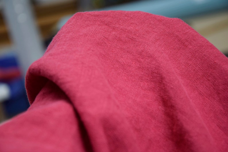 May include: A close-up of a soft, pink fabric with a textured surface. The fabric is folded and draped, creating a smooth, flowing look.