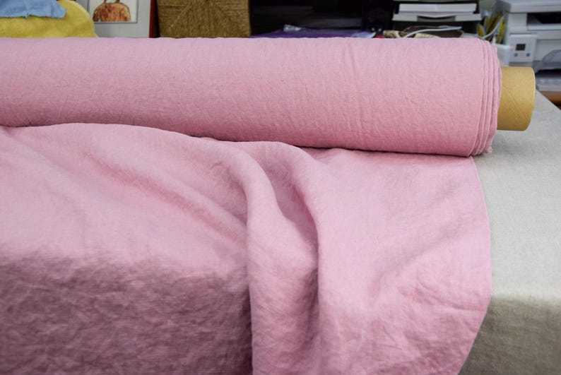 Puede incluir: Un rollo de tela rosa claro, con una textura suave y arrugada. Parte de la tela est&aacute; enrollada, el resto drapeada. El material parece ser de peso medio, adecuado para diversos proyectos de costura y manualidades.