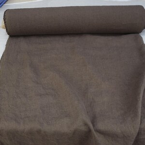 May include: A roll of dark brown fabric, partially unrolled, displaying a textured surface. The fabric is likely linen or a similar material, suitable for clothing or home decor projects.