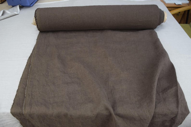 May include: A roll of dark brown fabric, partially unrolled, displaying a textured surface. The fabric is likely linen or a similar material, suitable for clothing or home decor projects.