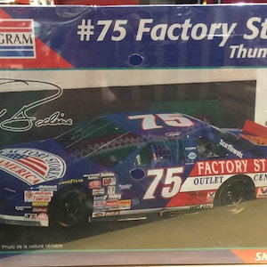 May include: A model car kit of a blue and red #75 Factory Stores Thunderbird race car. The box features a photo of the car and the driver,  #75,  and the words "Factory Stores Outlet Centers".