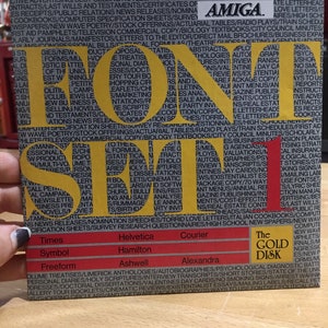 May include: A close-up of a yellow and black poster with the word "FONT" in large, bold letters. The poster lists various types of documents and publications, including instruction manuals, novels, movie scripts, and business presentations. The poster also includes the text "The Gold Disk" and the logo for Amiga.