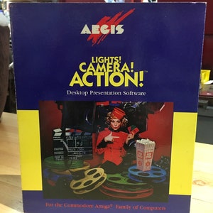 Puede incluir: Caja de software de presentación de escritorio Aegis Lights! Camera! Action! para la familia de computadoras Commodore Amiga. La caja presenta a una mujer con un vestido rojo y un sombrero, sosteniendo una claqueta y apuntando hacia la derecha. Hay carretes de película y un cubo de palomitas de maíz en el fondo.