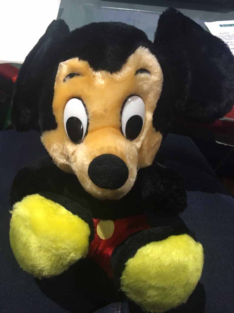 Pode incluir: Um brinquedo de pel&uacute;cia Mickey Mouse preto e amarelo com grandes orelhas pretas e uma camisa de bolinhas vermelhas e brancas.