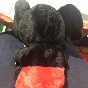 Pode incluir: Brinquedo de pel&uacute;cia preto com pele vermelha na parte inferior. O brinquedo tem orelhas grandes e um corpo redondo.