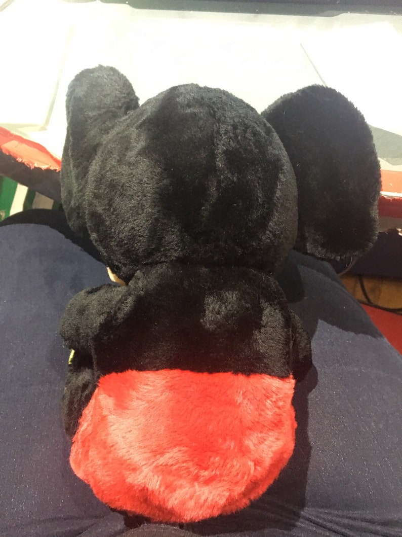 Pode incluir: Brinquedo de pel&uacute;cia preto com pele vermelha na parte inferior. O brinquedo tem orelhas grandes e um corpo redondo.