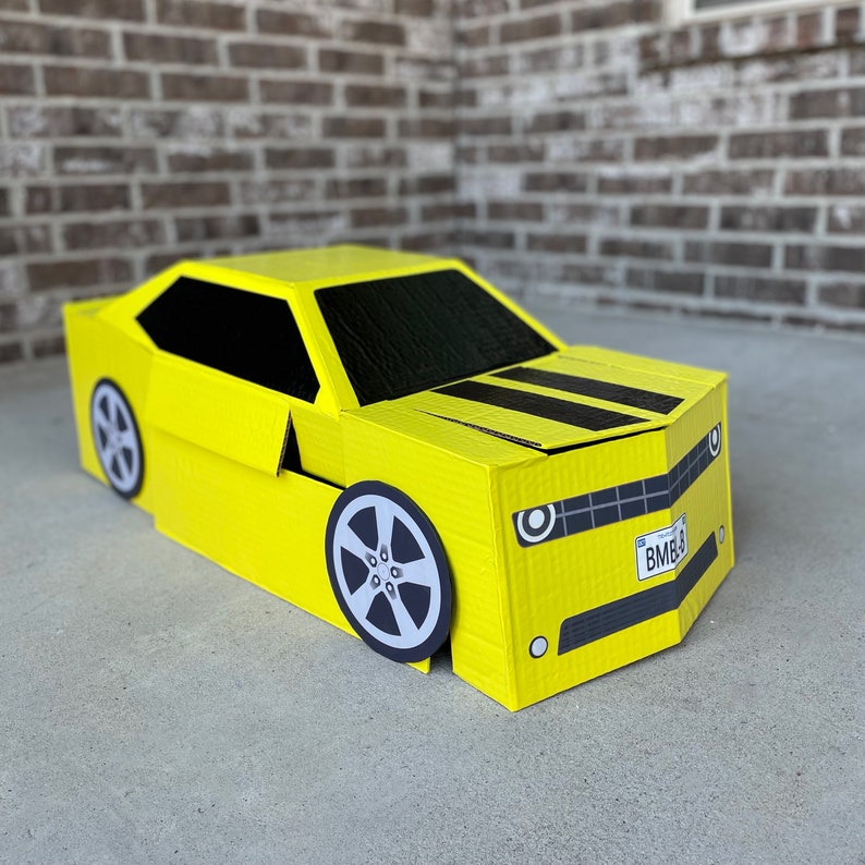 May include: A yellow cardboard car costume with black stripes and a license plate that reads "BMB9".