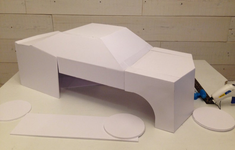 May include: A white foam board model of a car, with the body, wheels, and chassis all separate pieces. The model is being assembled on a white surface.