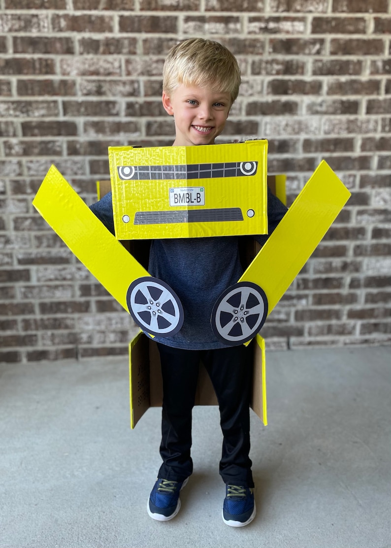 May include: A young boy wearing a yellow cardboard car costume. The costume has a license plate that reads "BMBl-B".