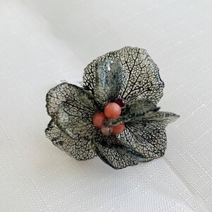 May include: A delicate black flower brooch with a cluster of pink and purple beads in the center.