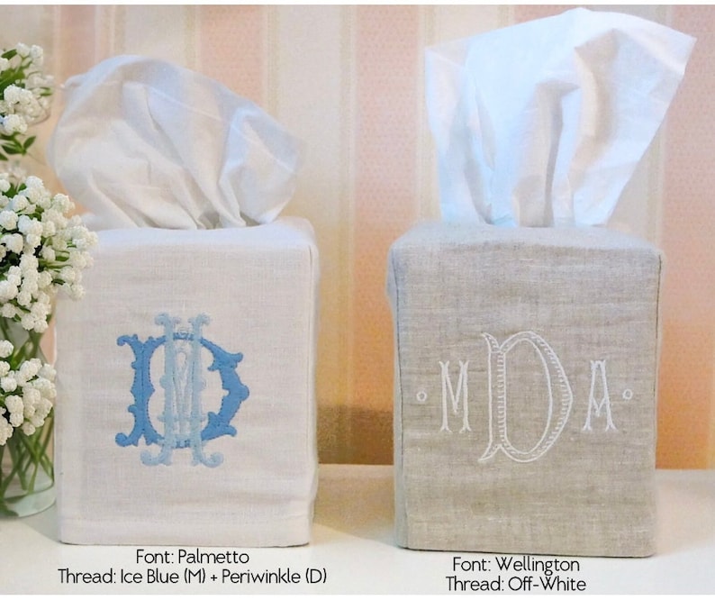 May include: Two square tissue box covers, one white with blue embroidery and the other beige with white embroidery. The white cover has the monogram "MD" in a Palmetto font with Ice Blue and Periwinkle thread. The beige cover has the monogram "MDA" in a Wellington font with Off-White thread.