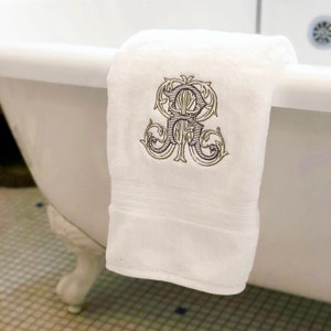 May include: White bath towel with a green and purple embroidered monogram of the letter "R" in a decorative font.