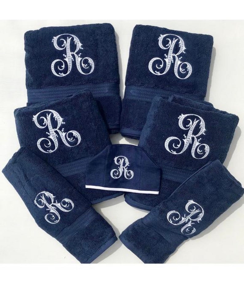 May include: Set of seven navy blue towels with white embroidered letter "R" in a decorative script. The set includes six bath towels and one hand towel.