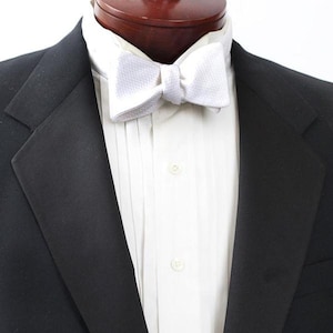 May include: A white bow tie with a textured pattern, worn with a white dress shirt and a black tuxedo jacket.