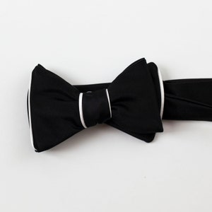 May include: A black bow tie with a white trim. The bow tie is made of a smooth fabric and has a classic design.