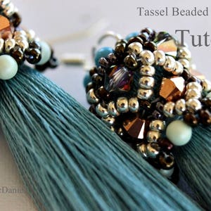 Può includere: Un paio di orecchini a nappa blu turchese con cime perlate. Le perle sono argentate, marroni e color rame con alcune perle trasparenti e iridescenti. Gli orecchini sono un progetto fai-da-te e l'immagine include il testo "Tassel Beaded Earrings Tutorial".