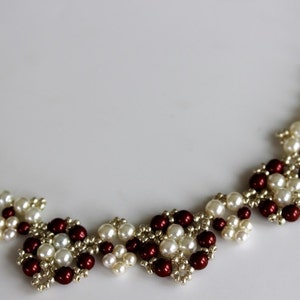 May include: A delicate necklace made with white and burgundy beads, arranged in a repeating pattern of small flower shapes.