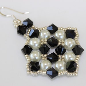 May include: A single beaded earring with a silver hook. The earring features a square design with alternating black faceted beads and white, round, pearl-like beads. The edges are lined with small silver beads.