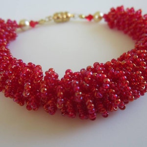 May include: A red beaded bracelet with a gold clasp. The beads are small and iridescent, creating a shimmering effect.