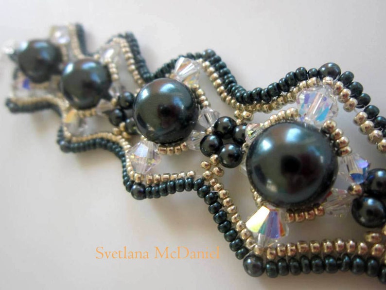 May include: A dark green and gold beaded bracelet with large black pearls. The bracelet has a wavy design and is made with small seed beads.