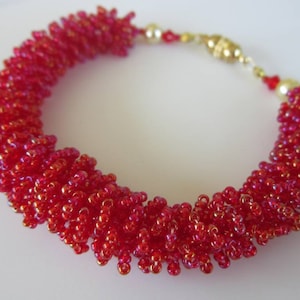 May include: A red beaded bracelet with a gold clasp. The beads are small and iridescent, creating a shimmering effect.