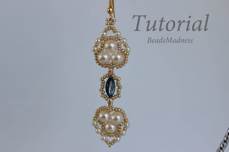 May include: Gold beaded earrings with a teardrop-shaped blue gemstone and white pearl accents. The earrings are hanging from a gold hook.