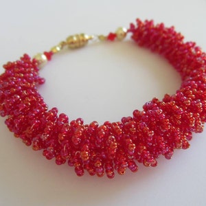 May include: A red beaded bracelet with a gold clasp. The beads are small and tightly packed, creating a textured look.