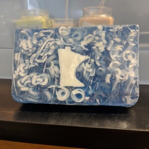 May include: A blue and white soap bar with a white outline of the state of Minnesota. The soap has a swirl design.